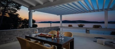 Un área de comedor al aire libre con una mesa preparada para dos, con vista a un cuerpo de agua y colinas.