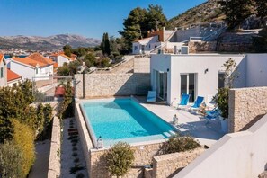 Eine moderne Villa mit Swimmingpool, Steinmauern und Blick auf die umliegende Landschaft.