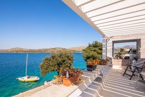 Ein Balkon mit Blick auf ein ruhiges Meer, ein Boot und Kübelpflanzen.