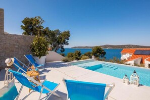 Ein Poolbereich mit Liegestühlen, einer Topfpflanze und Blick aufs Meer.