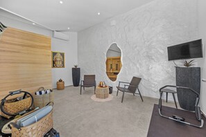 A modern interior with a wooden panel wall, a large stone wall with a TV, and a seating area with chairs and a small round table. - Villa Kim (Buje)