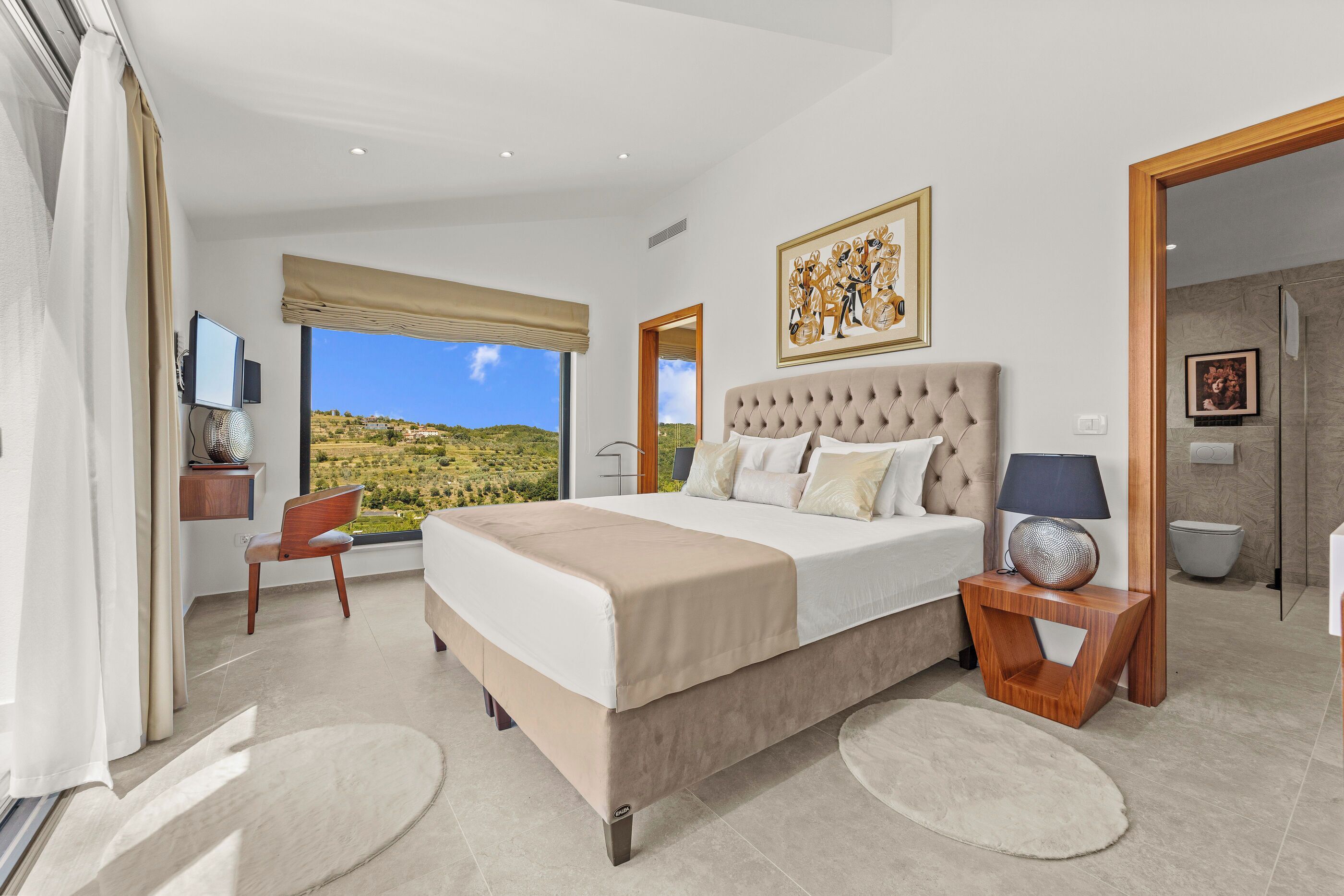 A bedroom with a large bed, a chair, a TV, and a view of the outdoors.