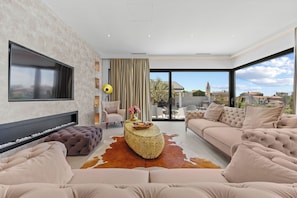 A modern living room with a large flat-screen TV, a fireplace, a sofa set, and a large window offering a city view. - Villa Kim (Buje)
