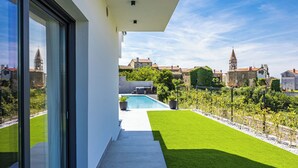 Ein modernes Gebäude mit Pool, Rasenfläche und Blick auf historische Bauten im Hintergrund.