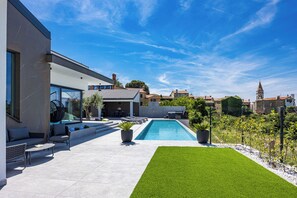A modern outdoor pool area with a clear blue sky, a well-maintained lawn, and a patio with seating. - Villa Kim (Buje)