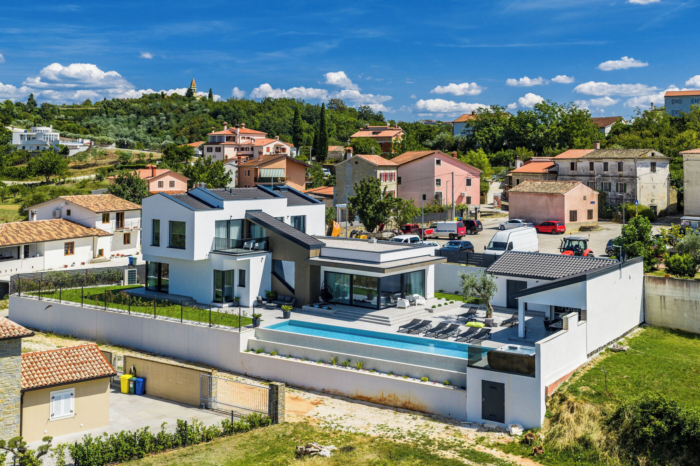 A modern house with a swimming pool, surrounded by other houses and greenery.
