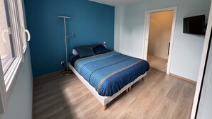 A bedroom with a bed, a floor lamp, a television on the wall, and a door leading to another room. - Vacation home 3 min from Le Mans 24H circuit with terrace, private garden, and Wi-Fi (Changé)