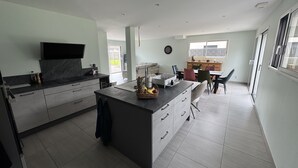 A modern kitchen with a central island, a dining area with chairs, and a large window providing natural light. - Vacation home 3 min from Le Mans 24H circuit with terrace, private garden, and Wi-Fi (Changé)