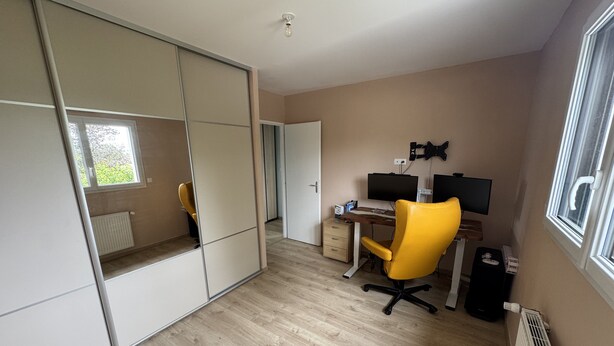 A room with a sliding door closet, a desk with a computer, a yellow office chair, and a radiator. - Vacation home 3 min from Le Mans 24H circuit with terrace, private garden, and Wi-Fi (Changé)