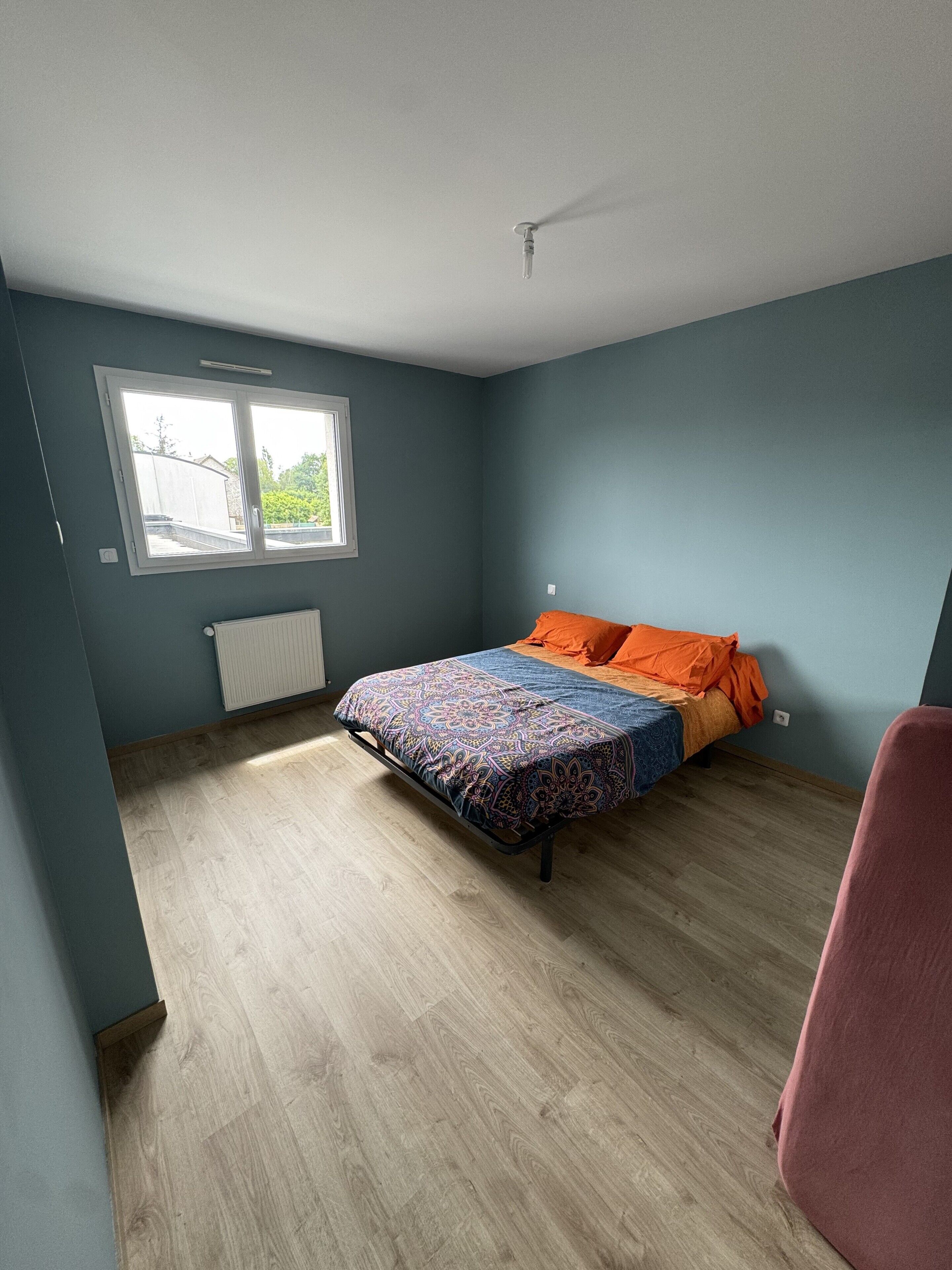 A bedroom with a bed, a window, a radiator, and a chair.