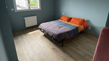 A bedroom with a bed, a window, a radiator, and a chair.