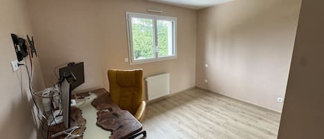 Una habitación con suelo de madera, un escritorio con computadora, una silla y un ventanal con vistas a árboles.