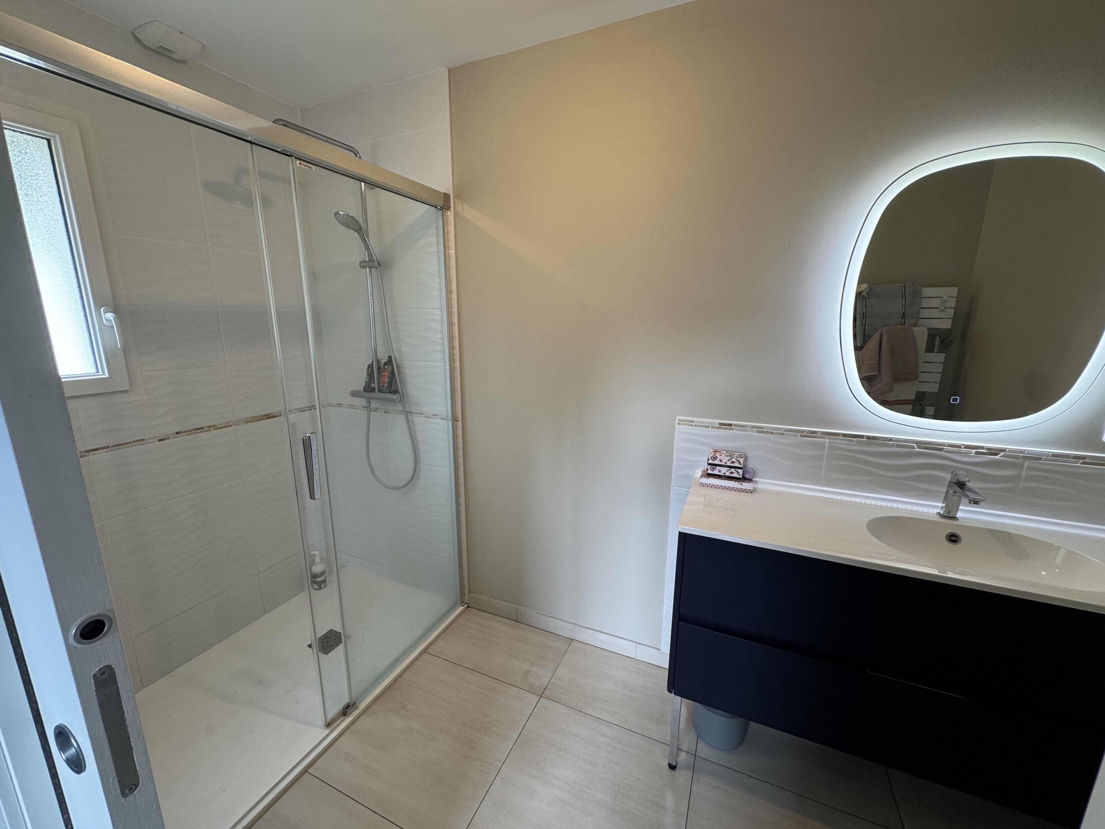 A modern bathroom with a glass-enclosed shower, a vanity with a mirror, and a light-colored tiled floor.