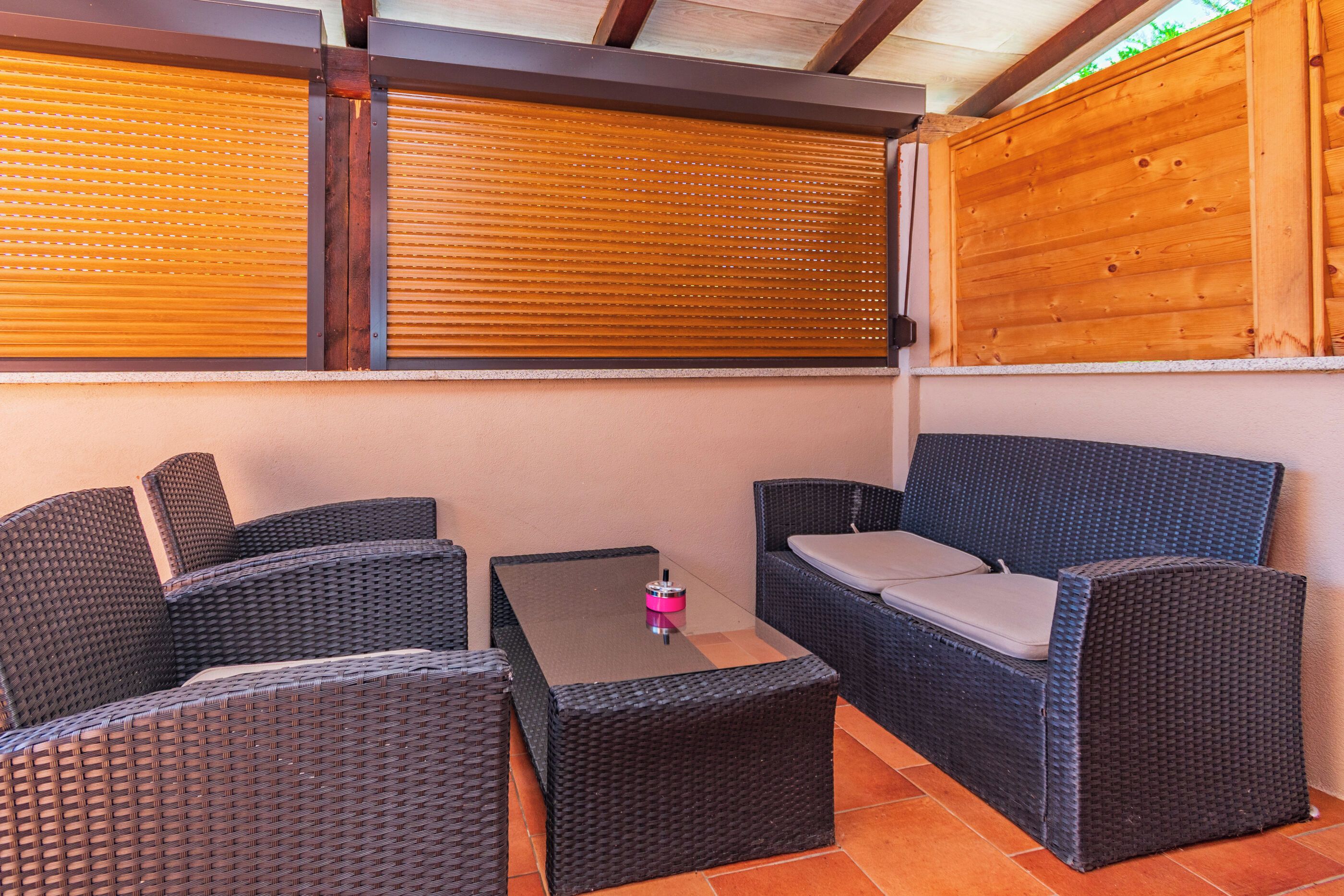 Un espacio de estar al aire libre cubierto con mobiliario de mimbre y una mesa, con techo y paredes de madera.