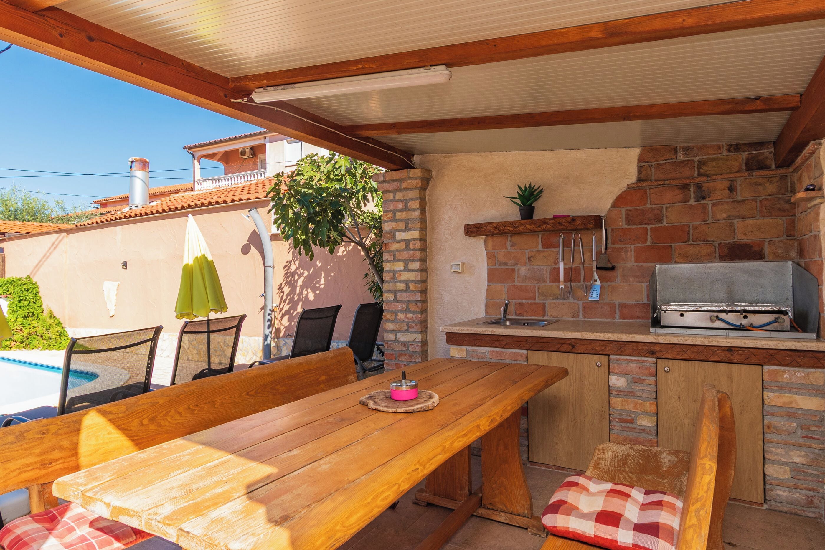 An outdoor kitchen area with a wooden table and chairs, a brick wall, and a grill.