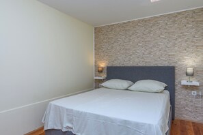A bedroom with a stone-patterned wall, a bed with white bedding, and two bedside lamps. - House Cancin (Porec)
