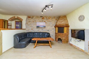 Un salon avec un canapé en cuir noir, une table basse en bois, un mur en pierre orné d’un tableau, une cheminée en briques et un téléviseur fixé au mur.