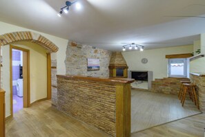 Ein Zimmer mit Steinwand, Kamin, Holzboden und Deckenventilator.