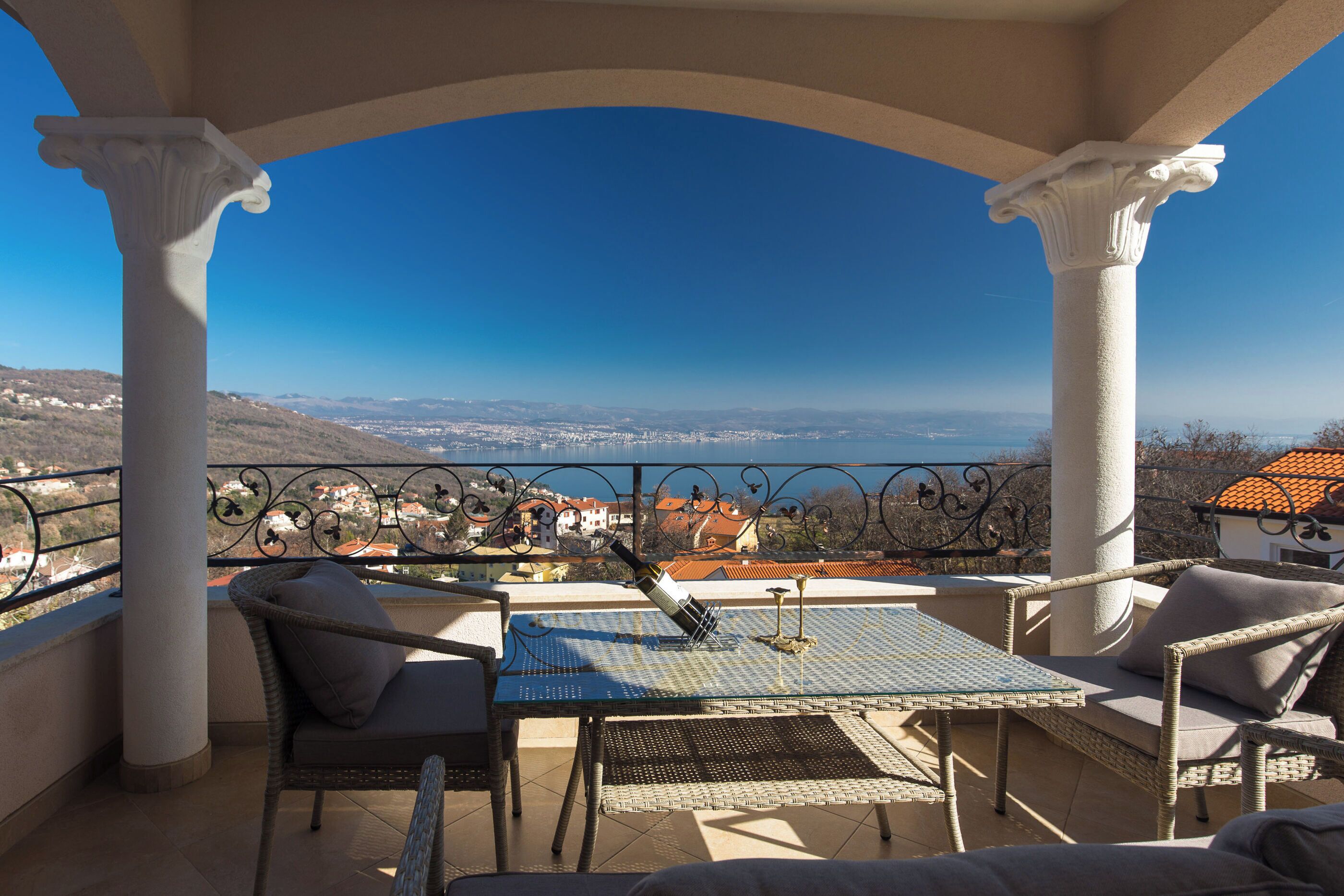 A balcony with a table and chairs, a view of a town, and a clear sky.