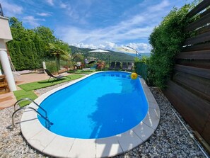 A swimming pool with a clear blue water, surrounded by a white tiled deck, and a wooden fence on one side. - Apartments Emily (Opatija)