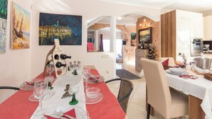 A dining area with a red tablecloth, white table, and various glassware. There are paintings on the walls and a kitchen in the background. - Apartments Emily (Opatija)