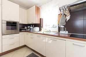 A modern kitchen with white cabinets, a built-in oven, a coffee maker, and a blender on the counter. - Apartments Emily (Opatija)
