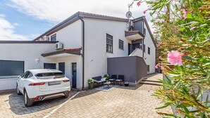 A modern two-story house with a car parked in the driveway, a satellite dish, and a small patio area with outdoor furniture. - Apartment Kovacic (Pula)