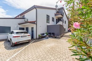 Ein modernes, zweistöckiges Haus mit einem Auto auf der Einfahrt, einer Satellitenschüssel und einer kleinen Terrasse mit Gartenmöbeln.