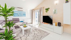 A modern living room with a sofa, coffee table, TV, and decorative plants. - Apartment Kovacic (Pula)