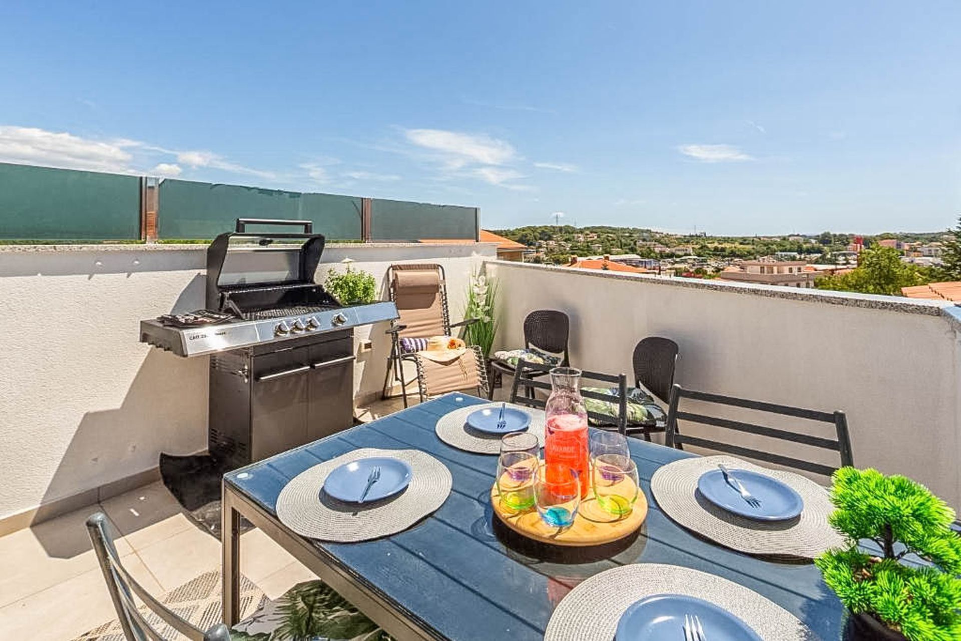 Une terrasse sur le toit équipée d’un barbecue, d’une table à manger, de chaises et offrant une vue sur la ville.