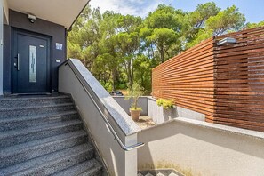 A staircase leading to a building with a dark door, a wooden fence, and a potted plant. - Apartment Kovacic (Pula)