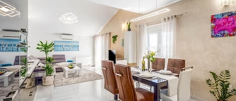 A modern dining area with a glass table, leather chairs, and a cityscape painting on the wall.