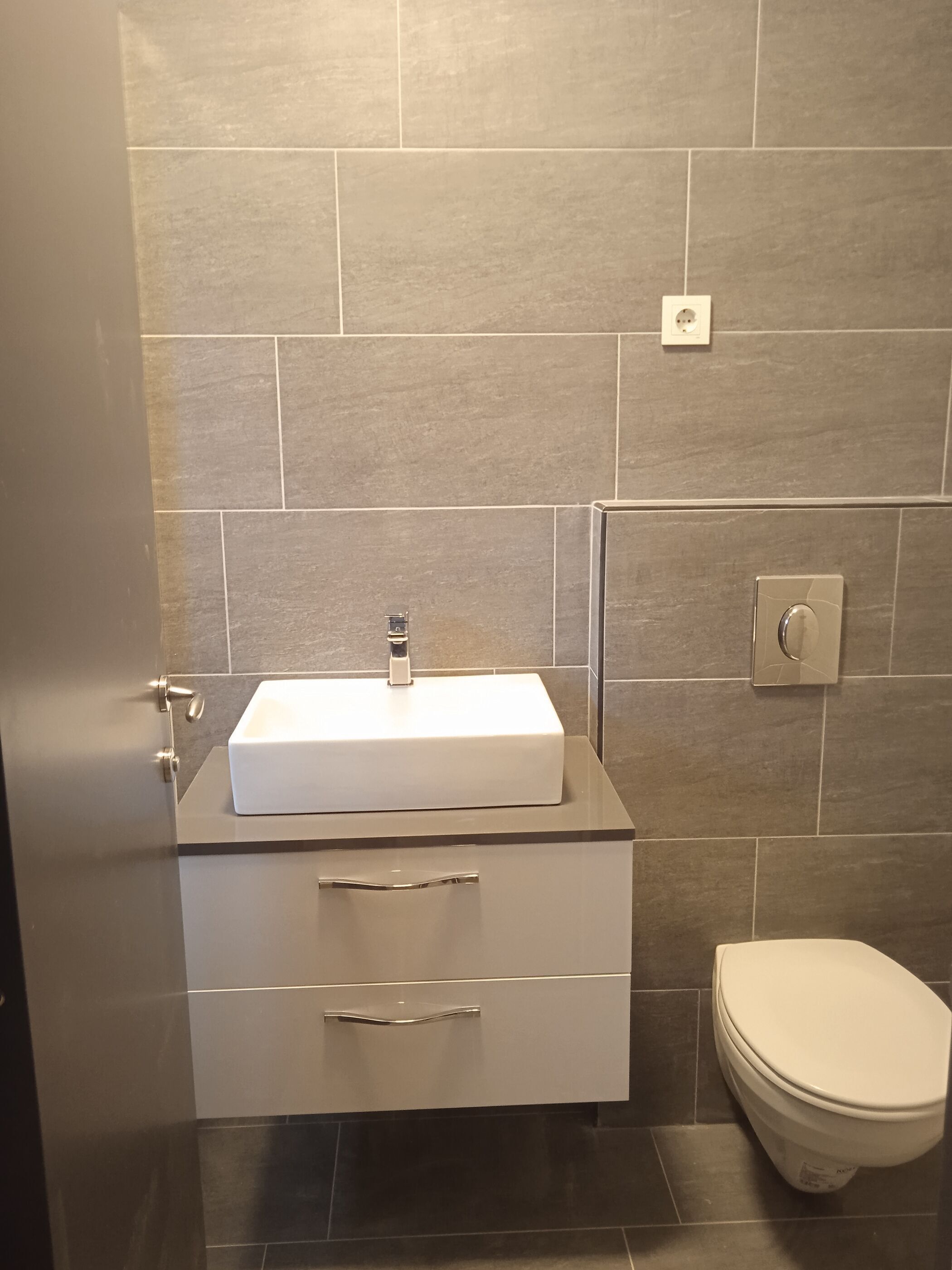 Un baño con un lavamanos blanco, un inodoro y una lámpara empotrada en la pared.