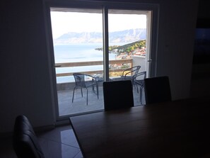 Quarto com porta de correr de vidro que dá para uma varanda com vista para um corpo d'água e montanhas.