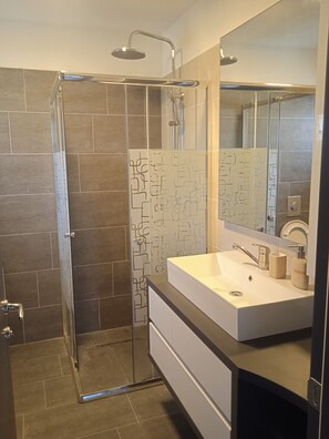 Uma casa de banho moderna com cabine de duche em vidro, lavatório branco com espelho e azulejos com padrão.