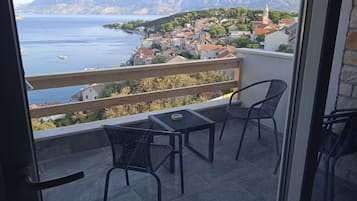 Un balcón con dos sillas y una mesa, con vistas a un pueblo costero con edificios y montañas al fondo.