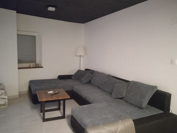 A living room with a grey sectional sofa, a wooden coffee table, a floor lamp, and a window with blinds. - Apartment Anton (Selca)