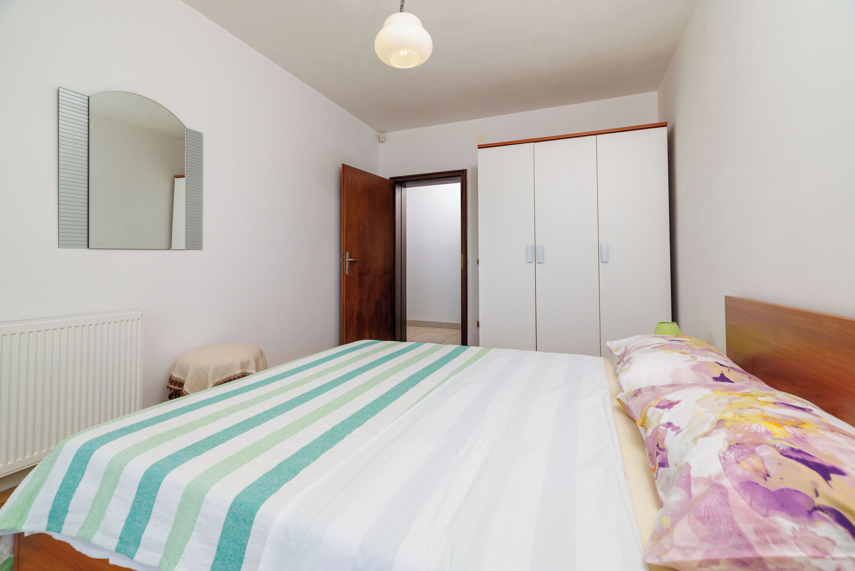 A bedroom with a bed, a mirror, a wardrobe, and a radiator.