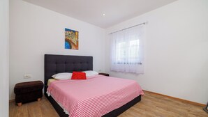 Ein Schlafzimmer mit einem Bett, einem Nachttisch, einem Fenster mit Vorhängen und einem Gemälde an der Wand.