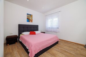 Ein Schlafzimmer mit einem Bett, einem Nachttisch, einem Fenster mit Vorhängen und einem Gemälde an der Wand.