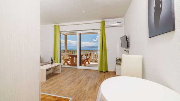 Ein Zimmer mit Balkon, einer Couch, einem Tisch und einem an der Wand befestigten Fernseher.