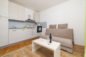 A compact kitchen with white cabinets, a built-in oven, and a dining table with a bottle and glasses. - Apartments Andrijanic (Crikvenica)