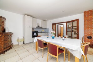 A dining area with a table set for four, a kitchen in the background, and a brick wall. - Apartments Andrijanic (Crikvenica)