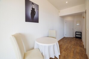 A room with a round table, a white chair, a wall-mounted picture, and a wooden floor. - Apartments Andrijanic (Crikvenica)