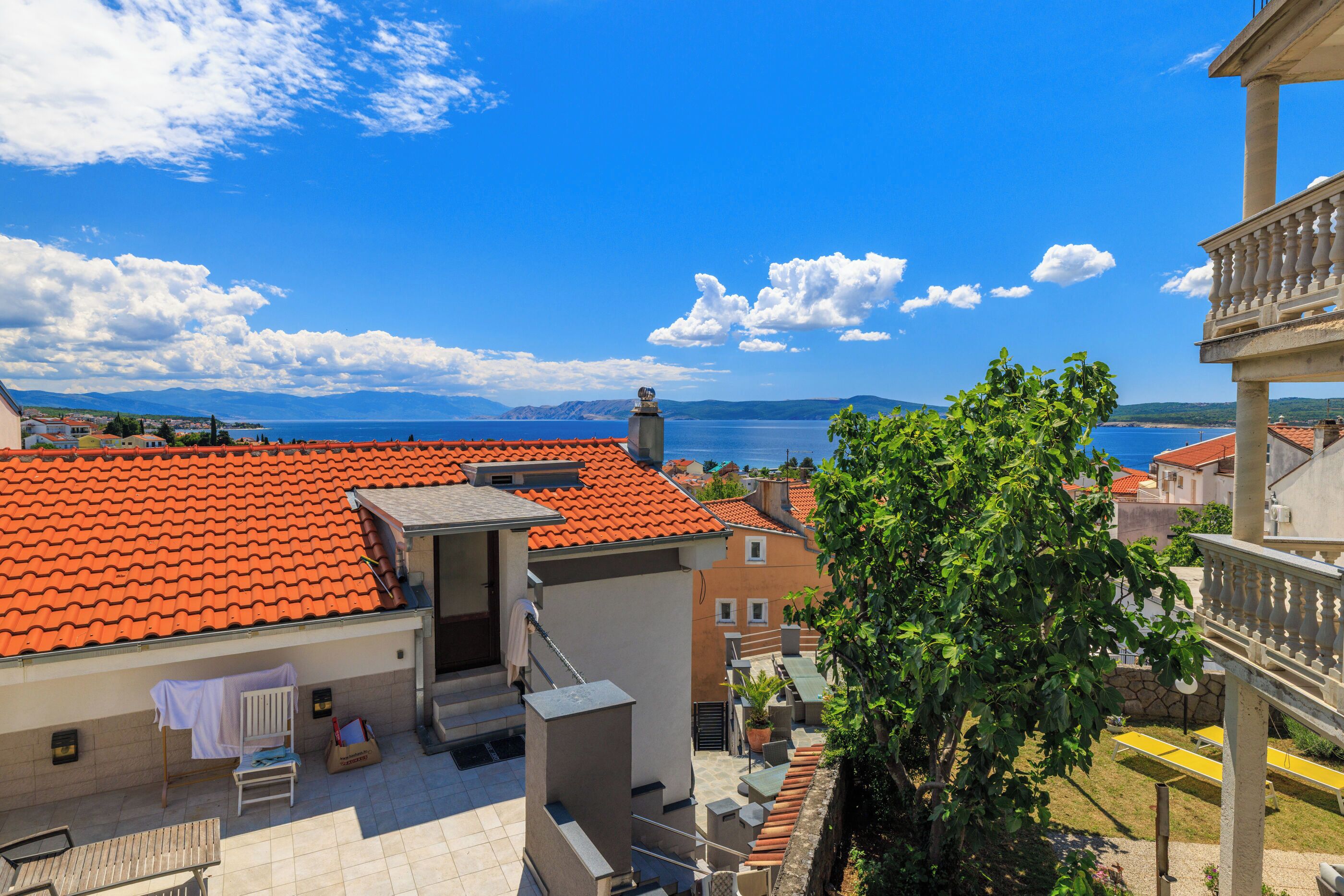 A residential area with red-tiled roofs, a balcony, and a view of the sea.
