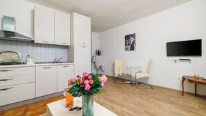 Eine moderne Küche mit weißen Schränken, einem Essbereich mit Tisch und Stühlen, einem Flachbildfernseher und einer Vase mit Blumen auf der Arbeitsplatte.