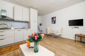 Eine moderne Küche mit weißen Schränken, einem Essbereich mit Tisch und Stühlen, einem Flachbildfernseher und einer Vase mit Blumen auf der Arbeitsplatte.