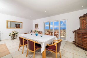 A dining area with a table set for four, chairs, a vase with flowers, a mirror, and a view of the sea through large windows. - Apartments Andrijanic (Crikvenica)