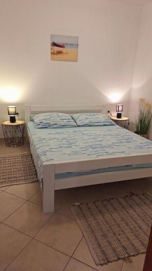 Une chambre à coucher avec un lit, deux tables de chevet, une lampe fixée au mur, une petite plante et un tableau accroché au mur.