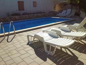 A swimming pool with lounge chairs and a stone wall. - Apartments Laura and Romano With Pool (Vir)